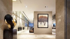 Un vestíbulo moderno con piso de mármol, una gran escultura abstracta y una obra de arte enmarcada con árboles.