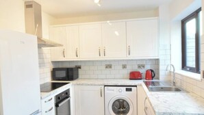 Une cuisine compacte avec des meubles blancs, un four à micro-ondes, une bouilloire rouge, un lave-linge et un évier.