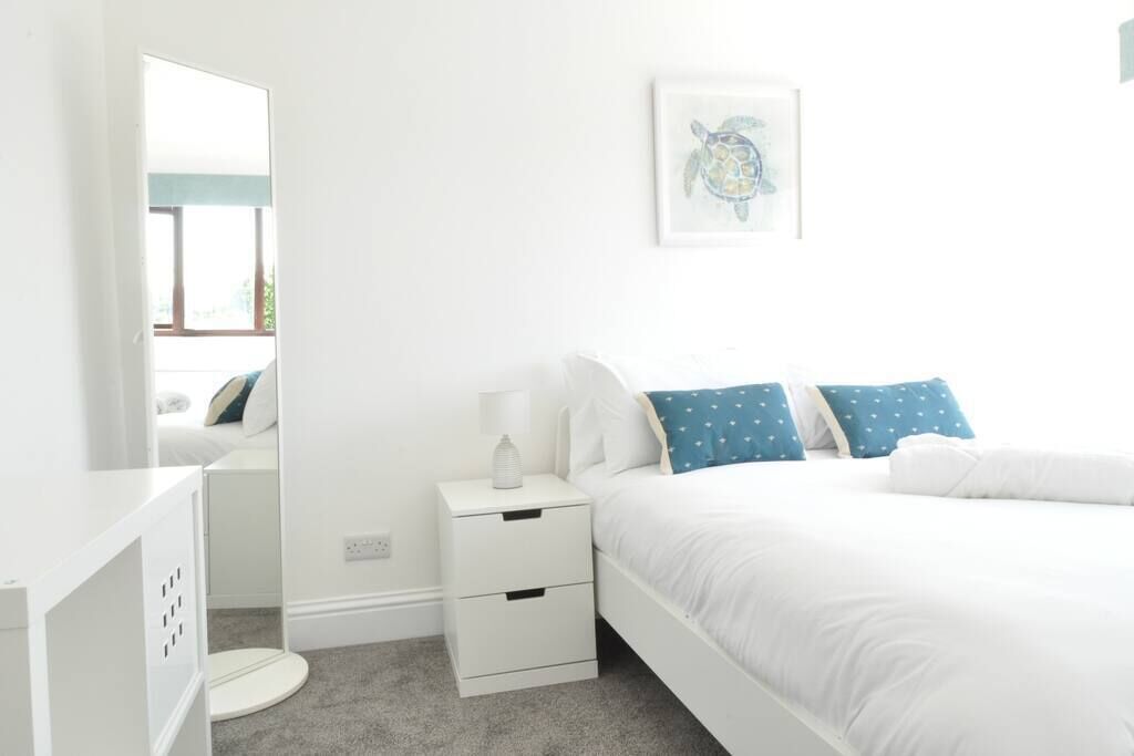 A bedroom with a bed, a nightstand, a mirror, and a wall-mounted picture.