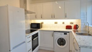Une cuisine compacte avec des meubles blancs, un four encastré, un four à micro-ondes, un lave-linge et un évier.