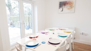 Uma sala de jantar luminosa com uma mesa branca posta para quatro pessoas, rodeada por cadeiras brancas.