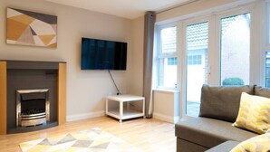 Un salon moderne avec une cheminée, un téléviseur à écran plat fixé au mur, un canapé avec des coussins et un tapis à motifs.