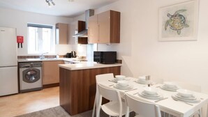 A modern kitchen with wooden cabinets, a built-in microwave, and a dining area with white chairs and a table set for four.