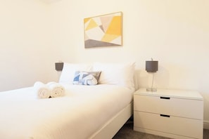 A neatly made bed with pillows, a bedside lamp, and a small bedside table with drawers.