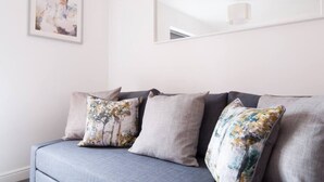 A modern living room with a grey sofa, floral cushions, a framed abstract painting, and a mirror on the wall.