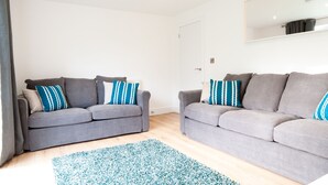 A modern living room with two grey sofas, a blue patterned rug, and a large mirror on the wall. - The Spitfire - Newly renovated 3-bed house in Cheltenham (Cheltenham)