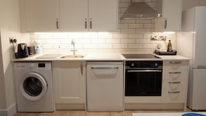 A modern kitchen with white cabinetry, a built-in washing machine, a dishwasher, and a stove. - The Spitfire - Newly renovated 3-bed house in Cheltenham (Cheltenham)