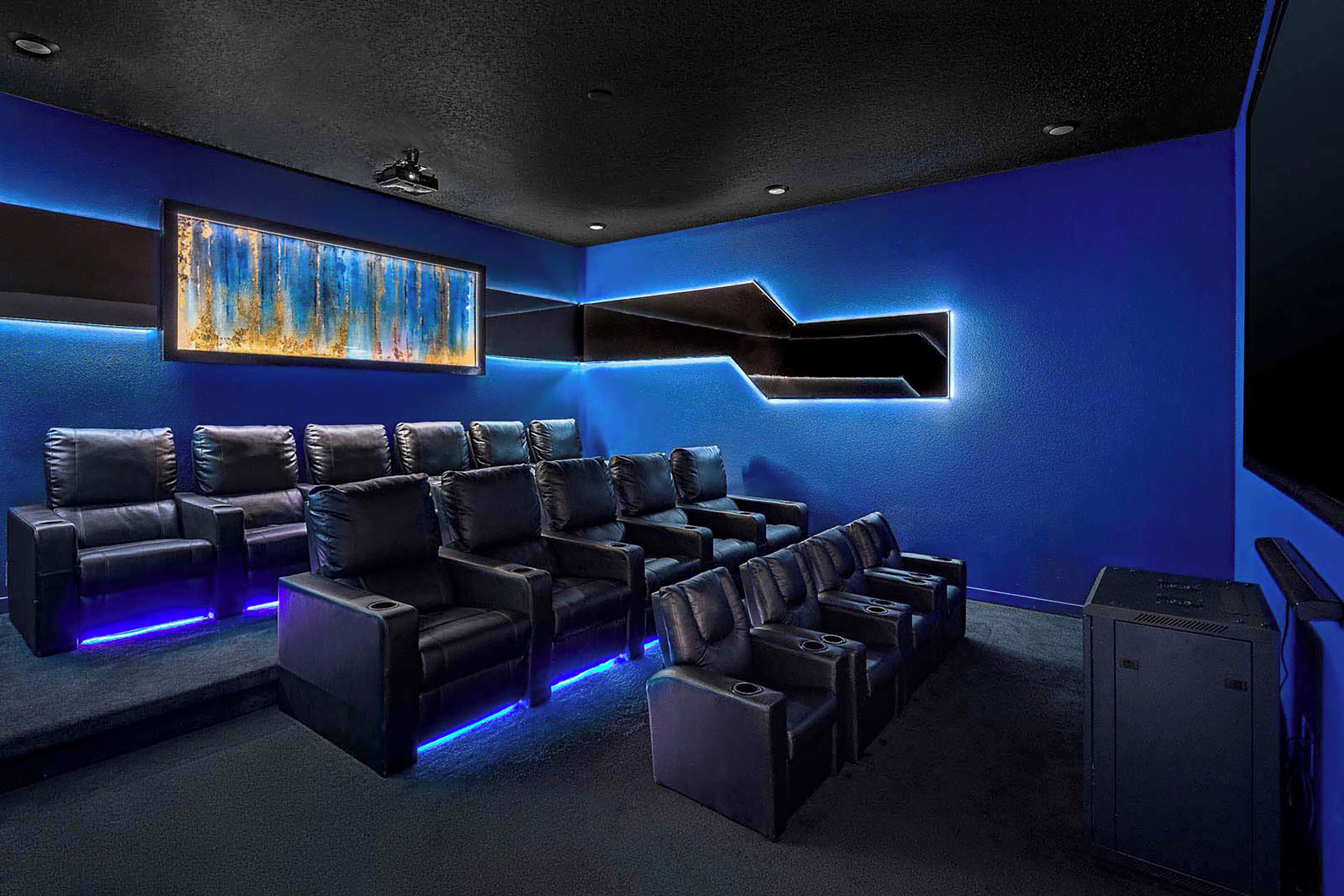 Une salle de cinéma privée avec un mur bleu, un grand écran et plusieurs fauteuils inclinables en cuir.