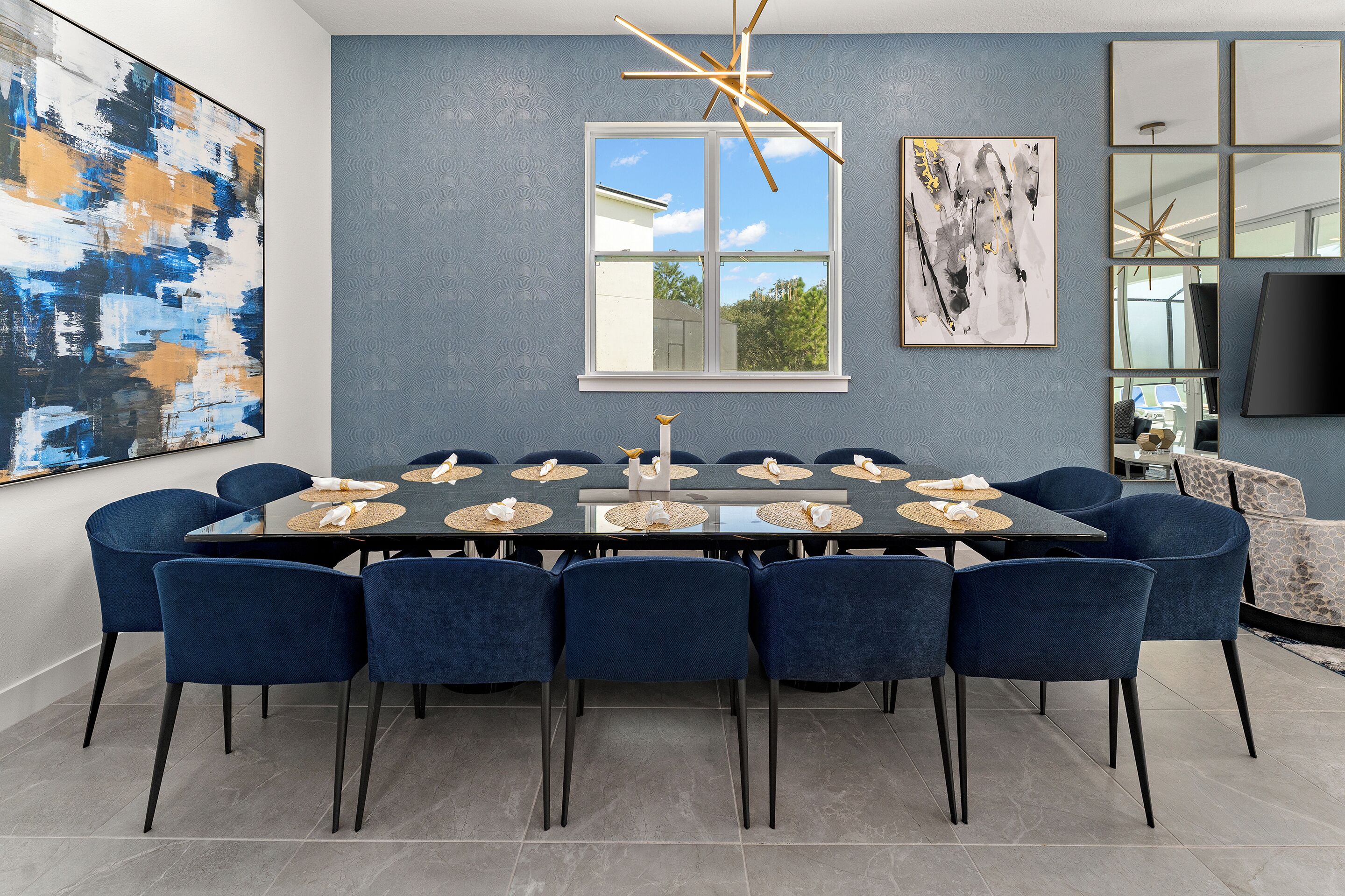 Una sala da pranzo moderna con un tavolo grande, sedie blu e opere d'arte astratte alle pareti.