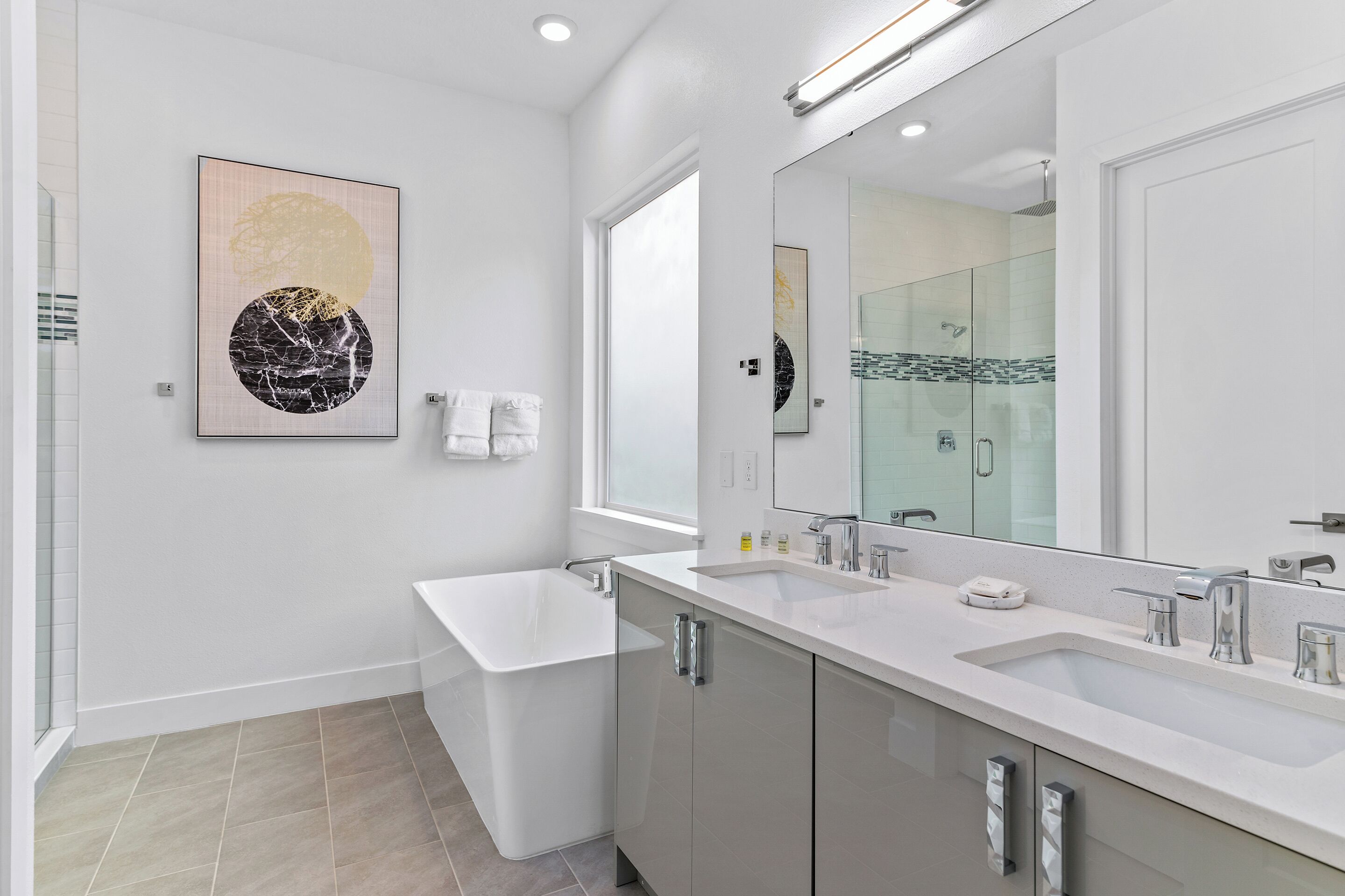 A modern bathroom with a large mirror, two sinks, a bathtub, and a toilet.