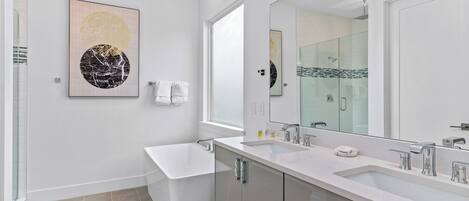 A modern bathroom with a large mirror, two sinks, a bathtub, and a toilet.