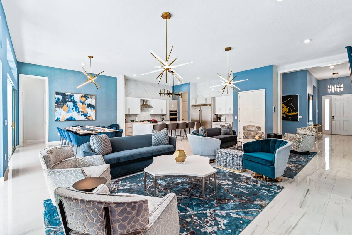 Ein modernes Wohnzimmer mit blauer Akzentwand, einem Essbereich und einer Küche im Hintergrund.