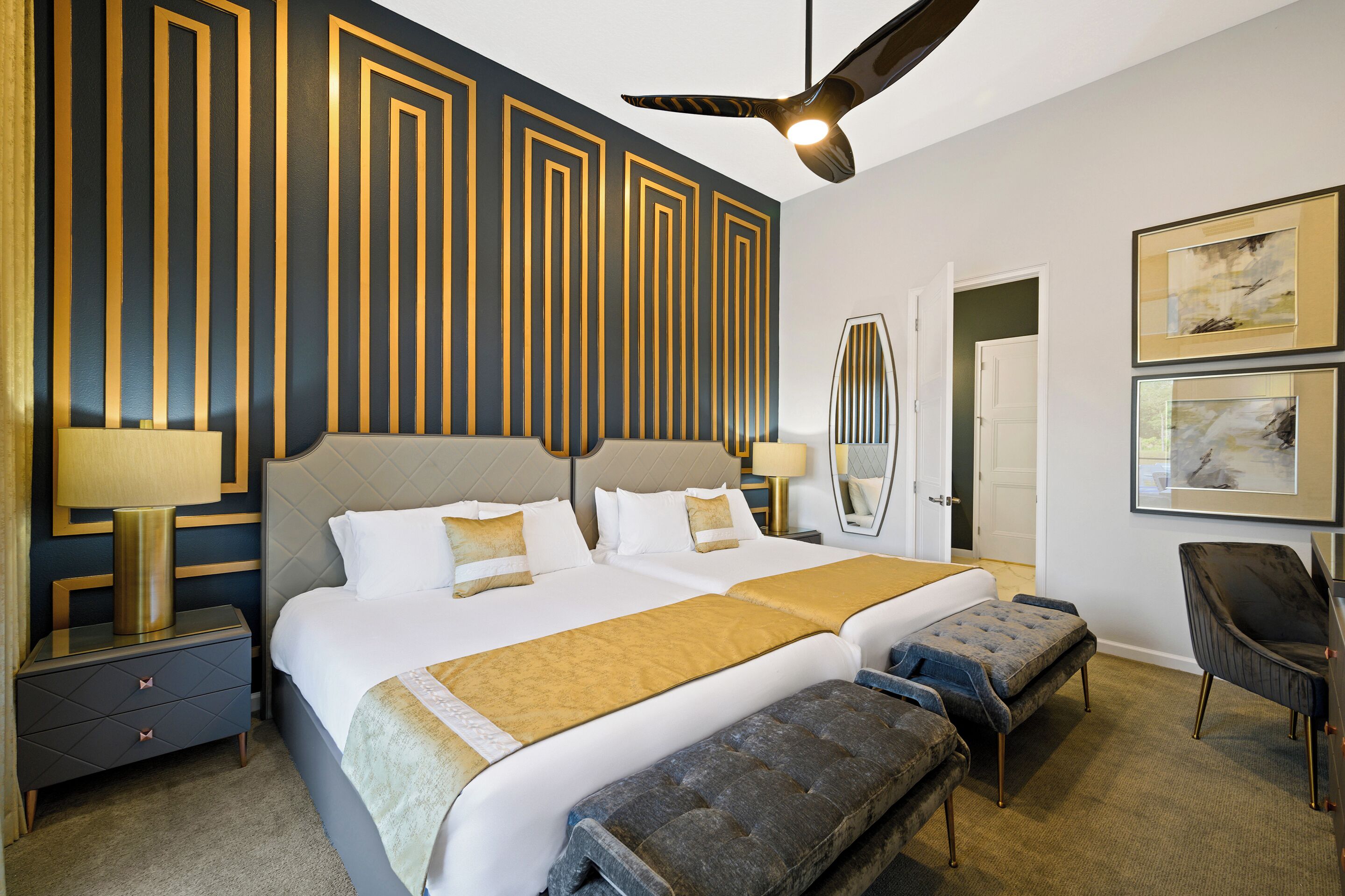 Quarto de hotel com uma cama grande, duas mesas de cabeceira, um ventilador de teto e obras de arte nas paredes.