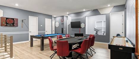 A modern room with a pool table, foosball table, and dartboard.