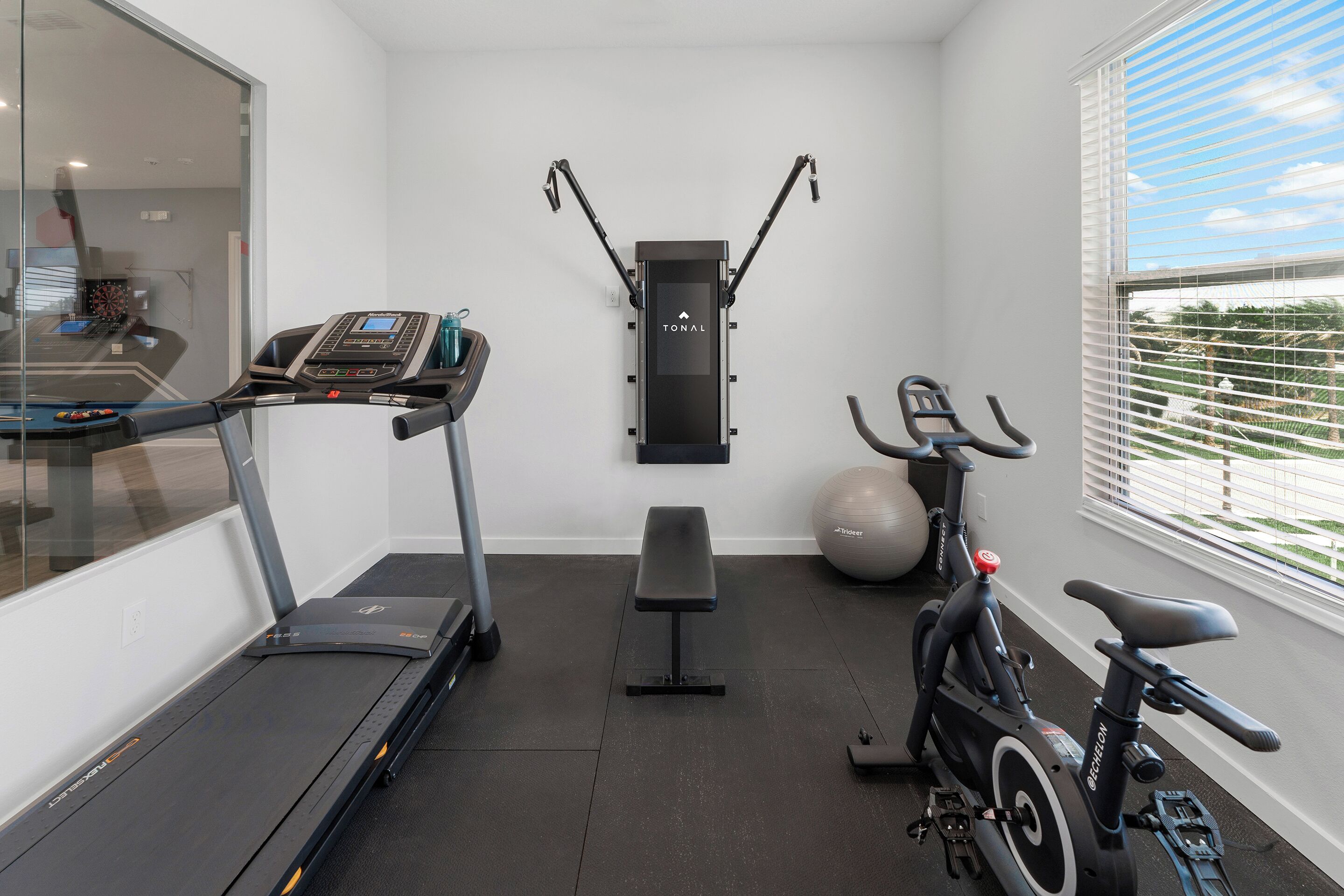 Une salle de sport à domicile équipée d’un tapis de course, d’un vélo d’appartement, d’un banc et d’un ballon d’exercice.