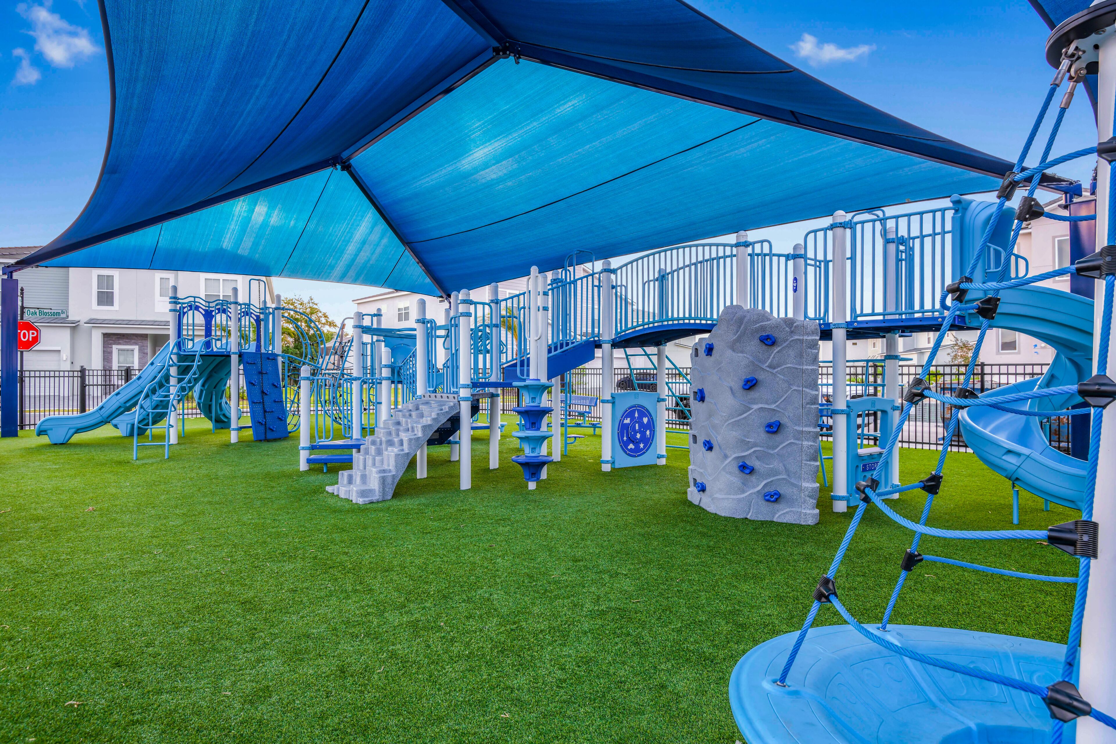 A playground with climbing structures and slides, surrounded by a blue canopy.