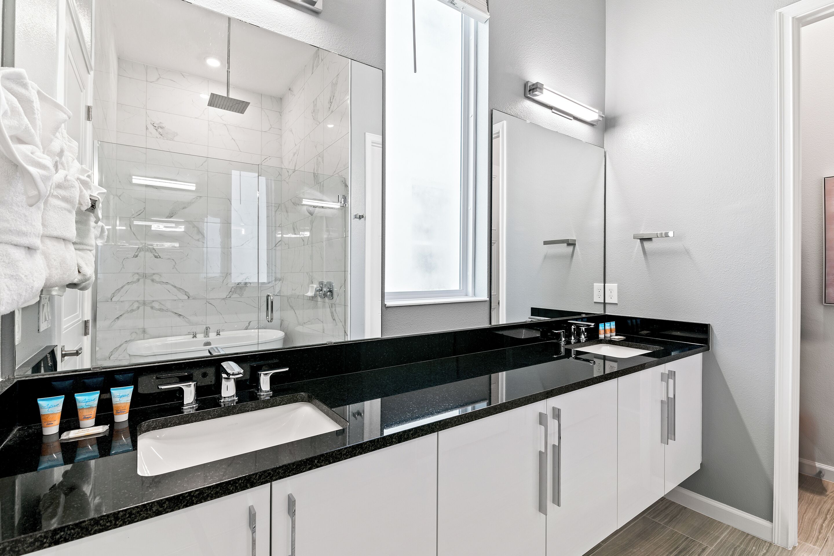 Une salle de bain moderne avec un plan de toilette noir, des meubles blancs, un grand miroir et une douche en verre.