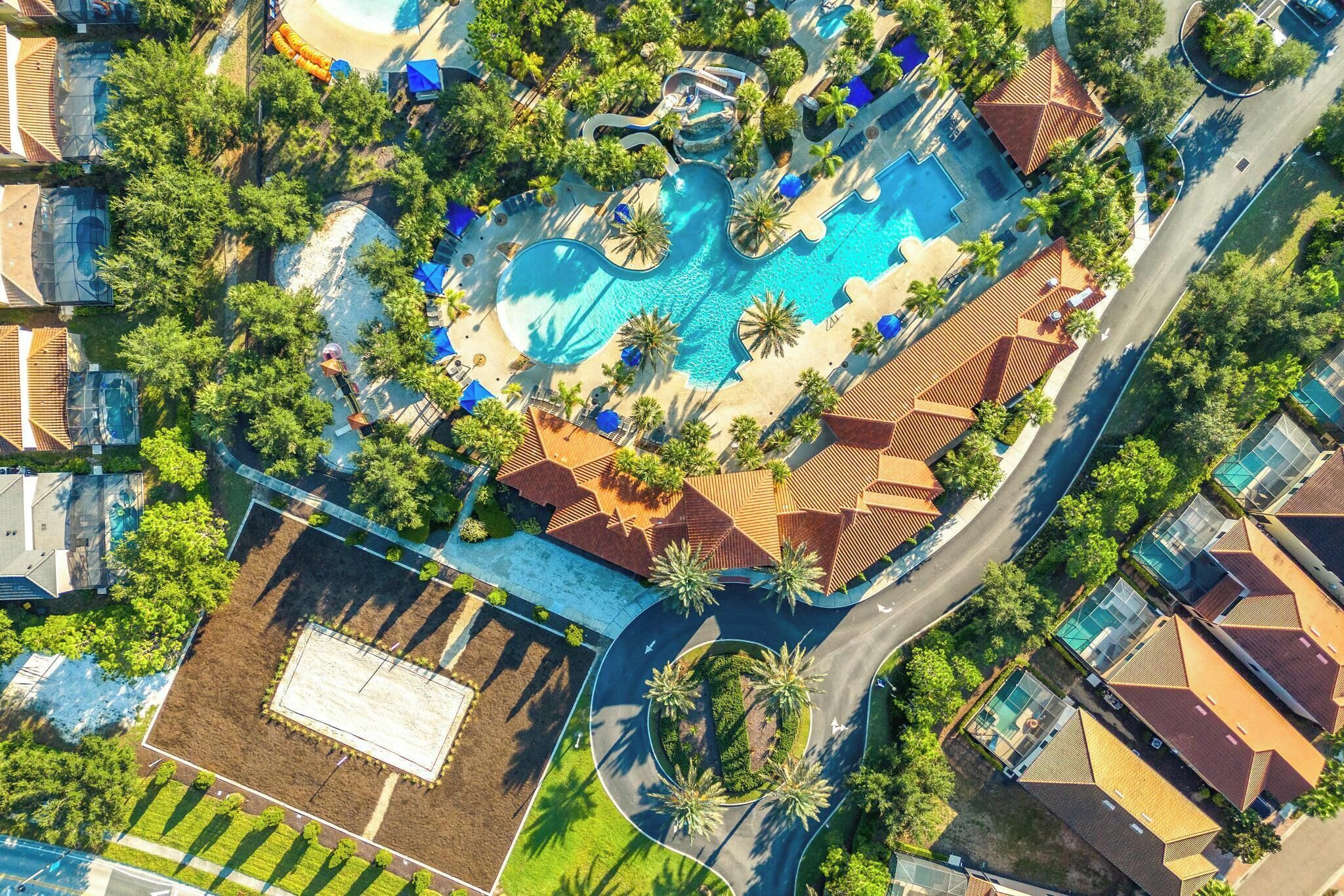 An aerial view of a resort with a central swimming pool, multiple guest villas, and surrounding greenery.