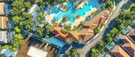 An aerial view of a resort with a central swimming pool, multiple guest villas, and surrounding greenery.