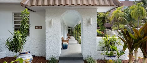 A pathway leading to a building with a tiled roof and a white exterior. There are potted plants and a bench along the path.