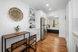 Una cocina compacta con armarios blancos, un refrigerador de acero inoxidable, una cafetera y un comedor con una mesa y sillas de madera.