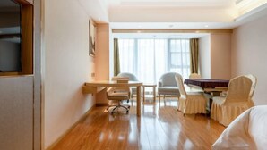 Una habitación de hotel con piso de madera, un escritorio, una silla, una cama y una ventana con cortinas.