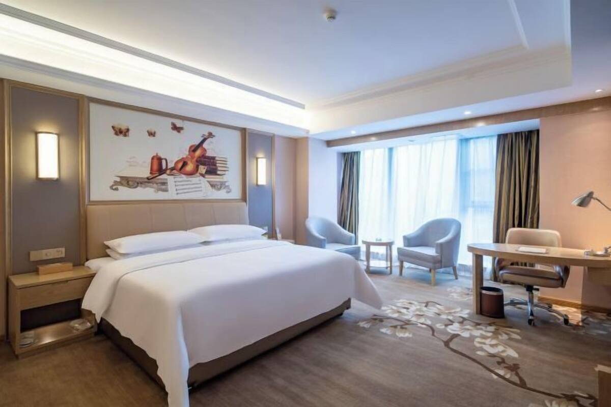 A hotel room with a large bed, a desk, two chairs, and a window with curtains.