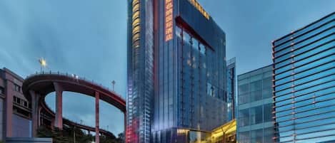 A modern high-rise hotel with a prominent glass facade, a curved pedestrian bridge, and a well-lit entrance area.