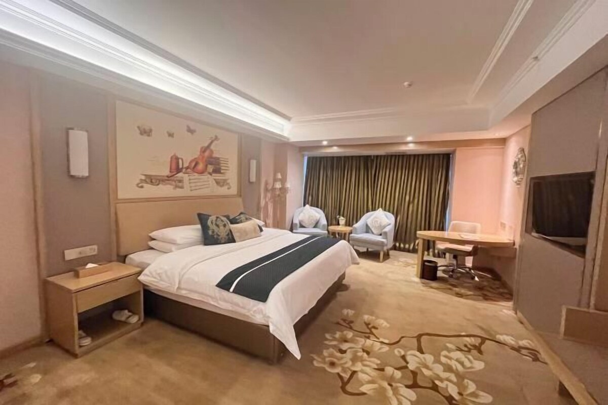 A hotel room with a bed, bedside table, chair, desk, and a television.