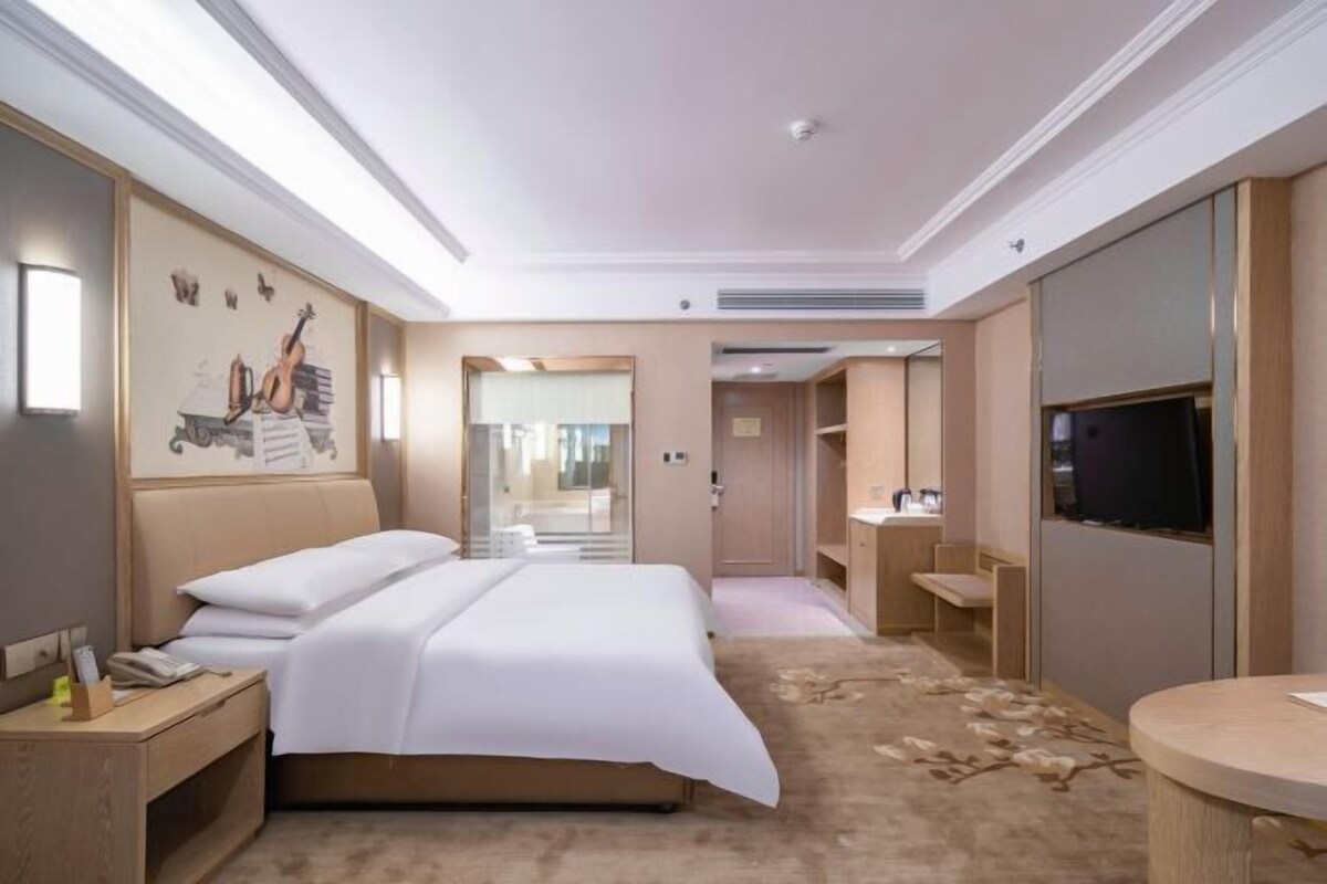 A modern hotel room with a large bed, a desk, a television, and a bathroom visible through a glass door.