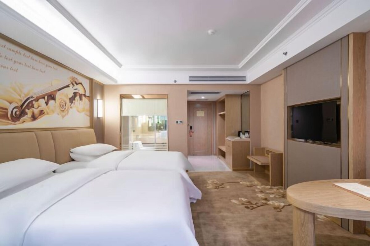 A hotel room with two beds, a television, a desk, and a large window.