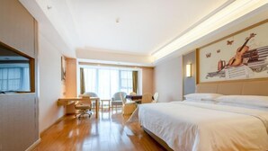 Una habitación de hotel con una cama grande, un escritorio, una silla y un ventanal con luz natural.