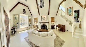 A spacious living room with a white sofa, a fireplace, a staircase, and a large window.