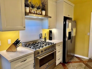 A kitchen with white cabinets, a stainless steel stove, a refrigerator, and a countertop with a knife block.