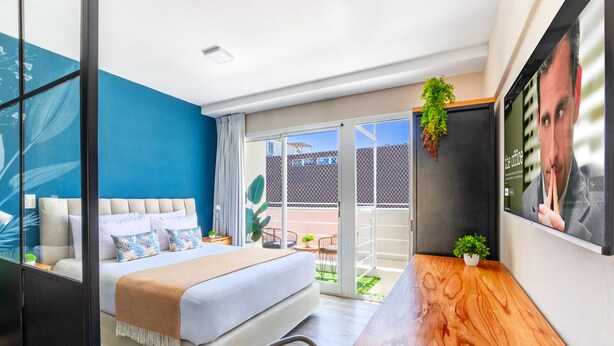 Et moderne hotelværelse med seng, træskrivebord, balkon med udsigt og et ophængt tv.