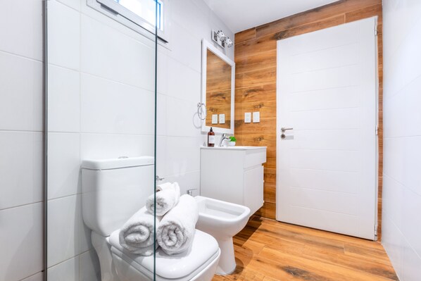 Un baño moderno con cabina de ducha de vidrio, inodoro, bidé y pared de acento de madera.
