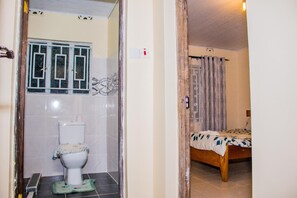 Une salle de bain avec des toilettes, une douche et un lit dans la pièce adjacente.