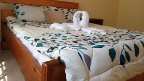 A neatly made bed with a floral bedspread, a wooden headboard, and a pair of towels arranged in a swan shape on the bed.