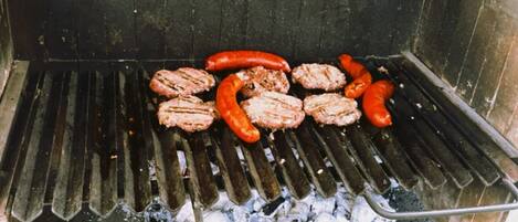 Ein Grill mit Bratwürsten und Frikadellen, die über Holzkohle gegrillt werden.