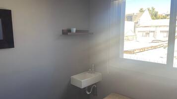 Casa de banho com lavatório branco, toalha e janela com vista para edifícios.