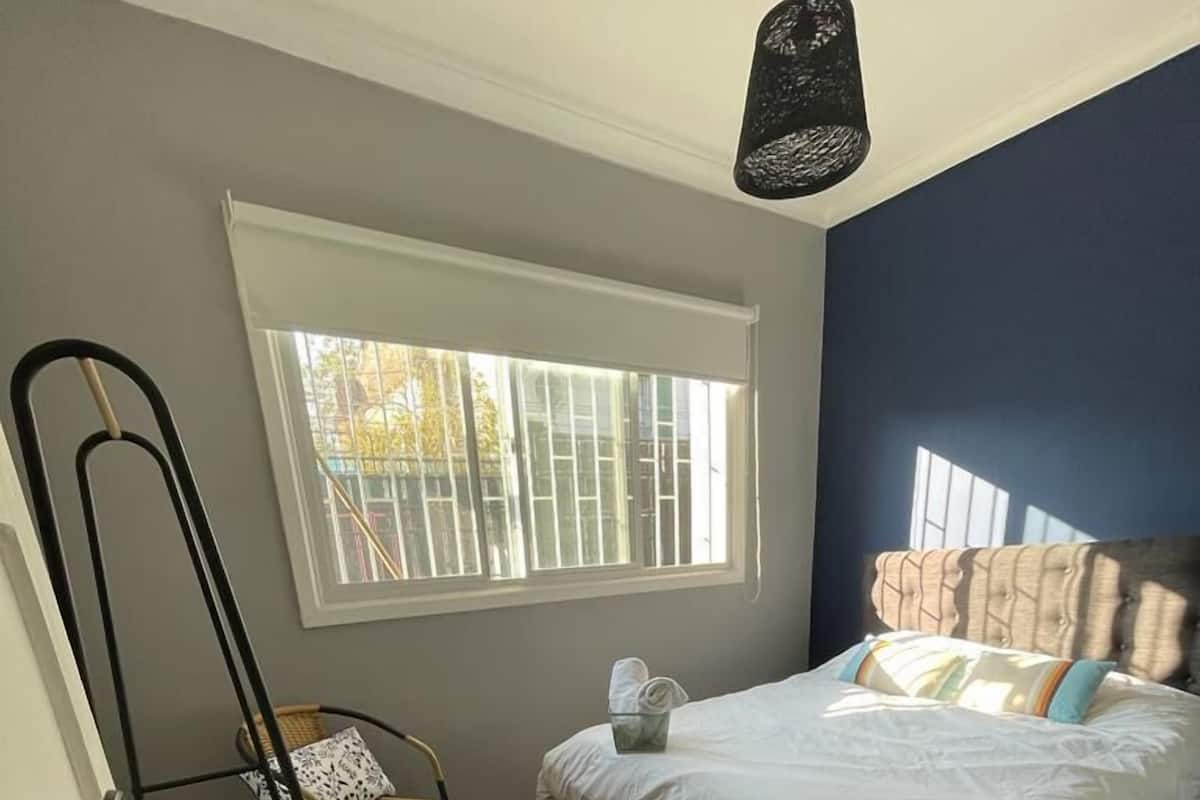 Une chambre à coucher avec un lit, une valise, une chaise et une fenêtre avec des stores.
