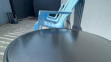 Una mesa redonda con estructura metálica, ubicada al aire libre junto a una silla de plástico azul y un tenedor.