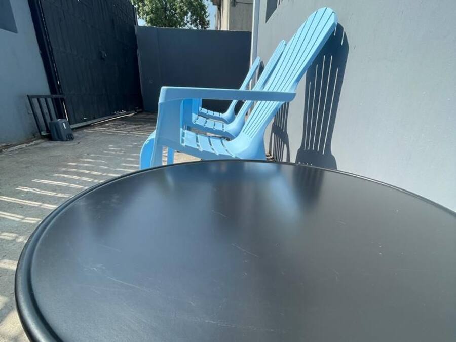 Una mesa redonda con estructura metálica, ubicada al aire libre junto a una silla de plástico azul y un tenedor.