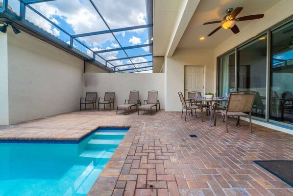 Un patio techado con piscina, mobiliario exterior y ventilador de techo.