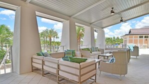 Un espacio de estar al aire libre cubierto con sofá, sillas y una mesa, con vista a una piscina y palmeras.