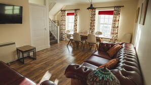 Un salon avec un canapé en cuir marron, une table à manger avec des chaises et un téléviseur fixé au mur.
