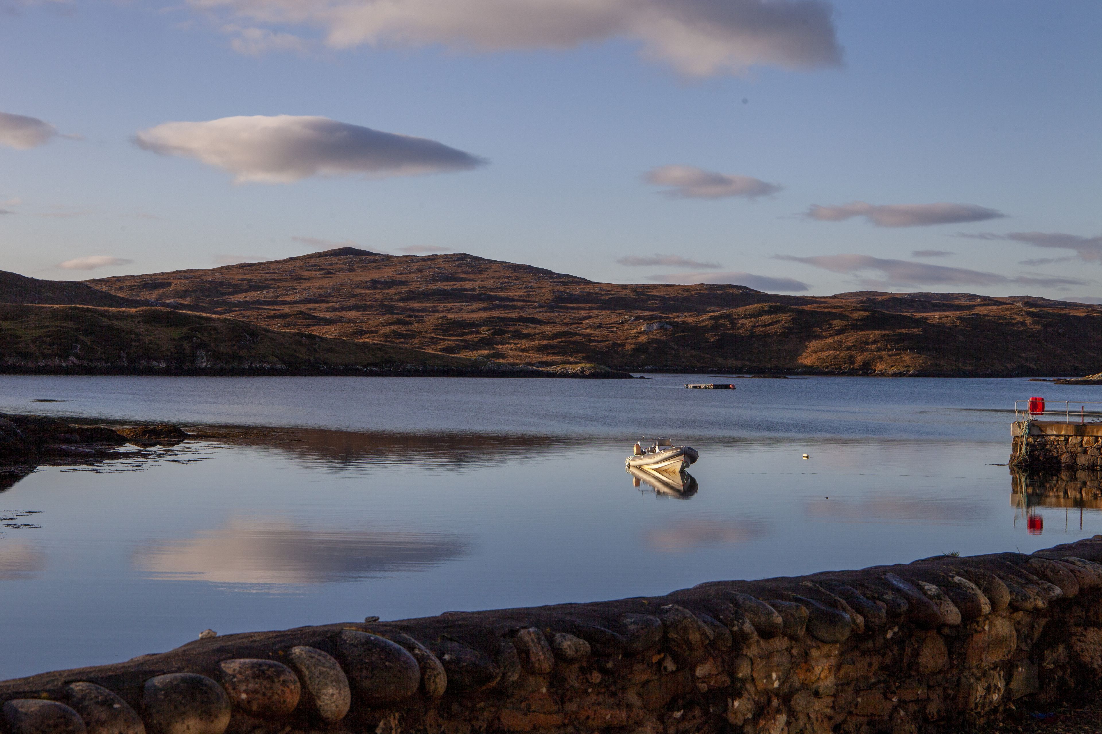 A calm lake with a small boat anchored near a stone wall.