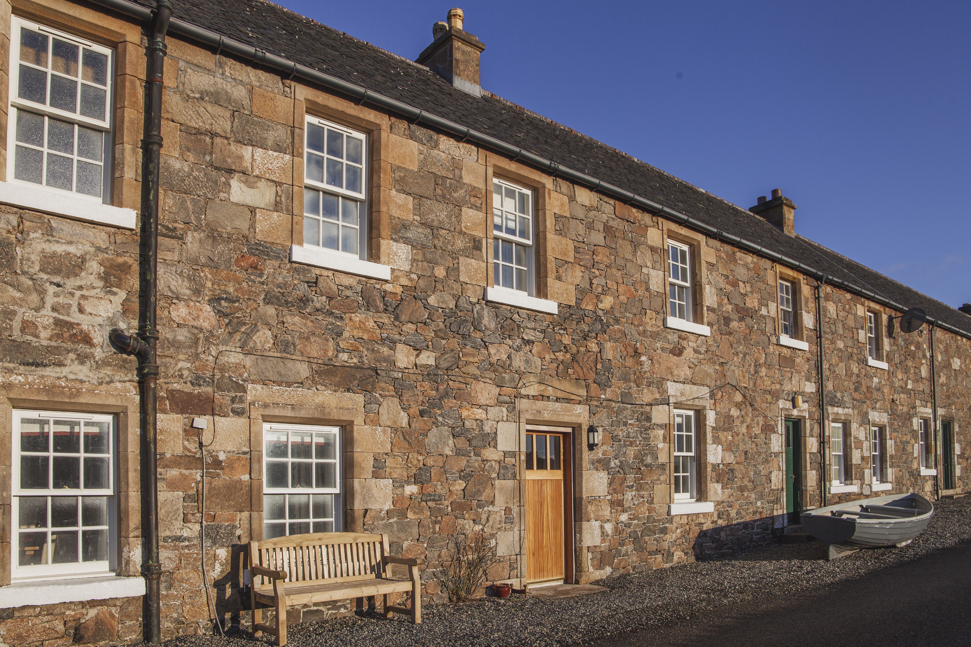 A stone building with multiple windows and doors, a bench outside, and a boat on the ground.