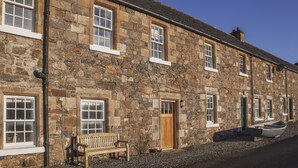 A stone building with multiple windows and doors, a bench outside, and a boat on the ground. - Castle Cottage - sleeps 6 guests  in 3 bedrooms (Tarbert, Isle of Harris)