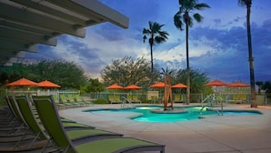 A pool area with lounge chairs and umbrellas, surrounded by palm trees and a cloudy sky. - Super Bowl Week! (Phoenix)